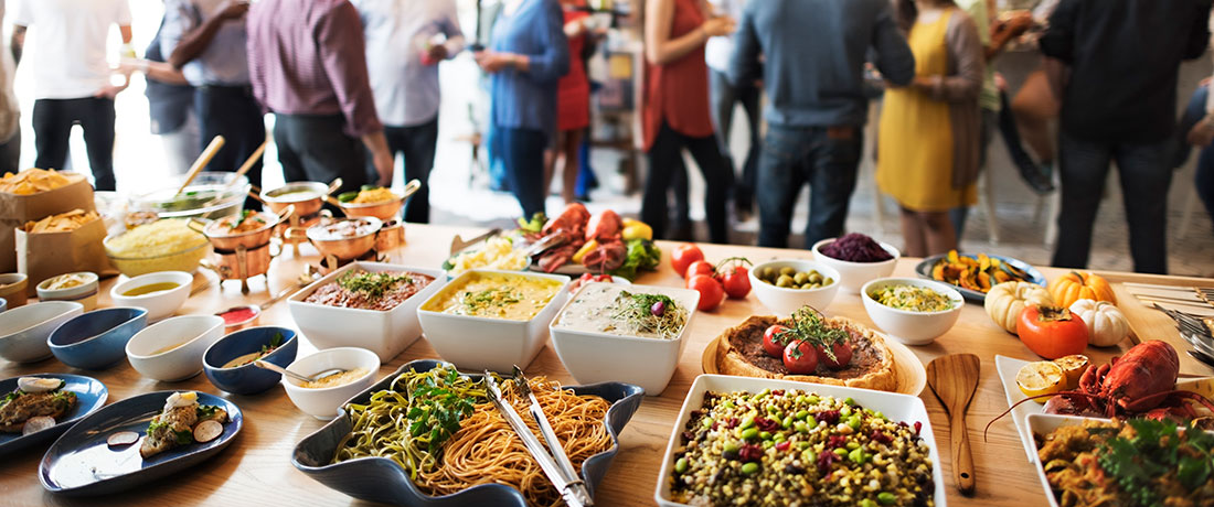 A lunch buffet of spreads, salads and finger foods, with people mingling in the background