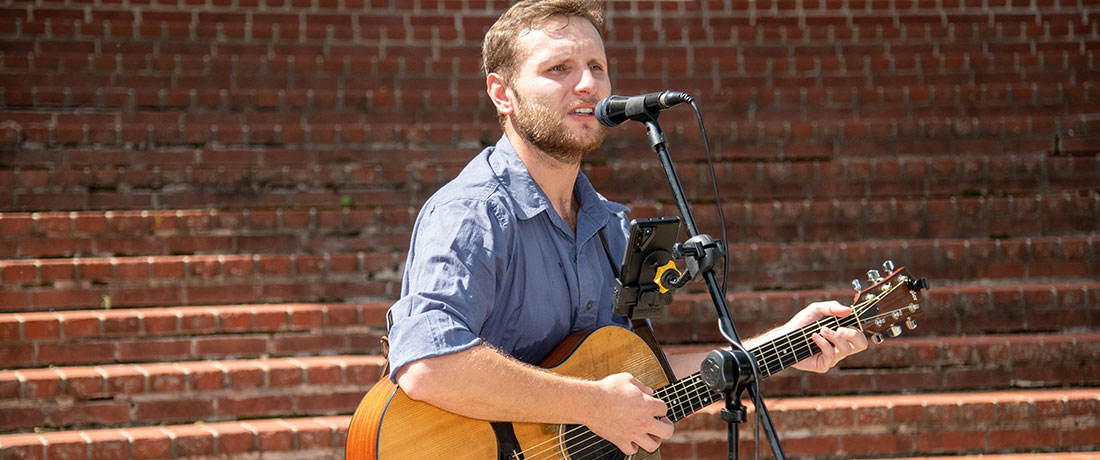A man playing guitar and singing outdoors during Parents and Family Weekend