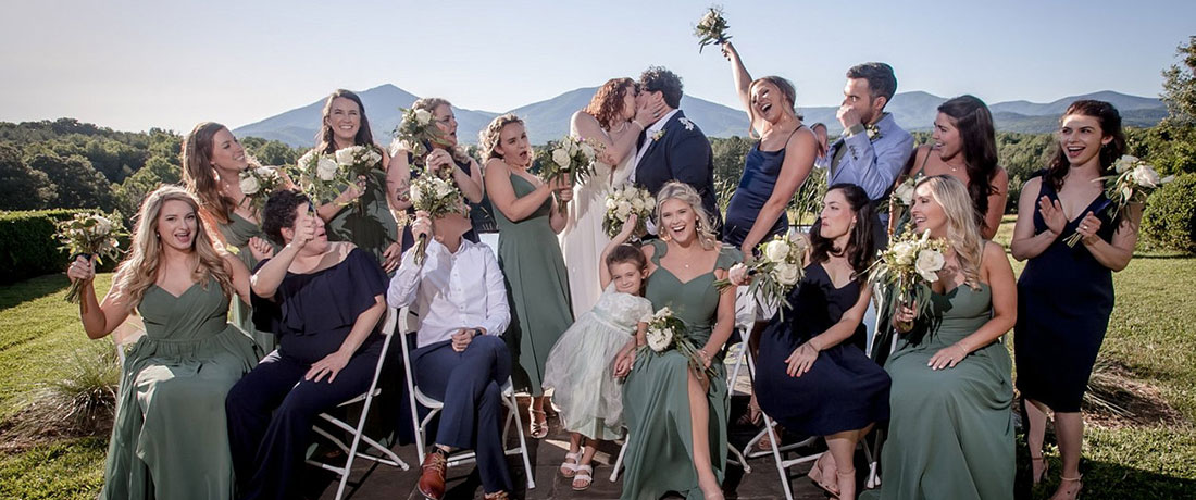 An outdoor wedding party cheers the happy couple as they kiss